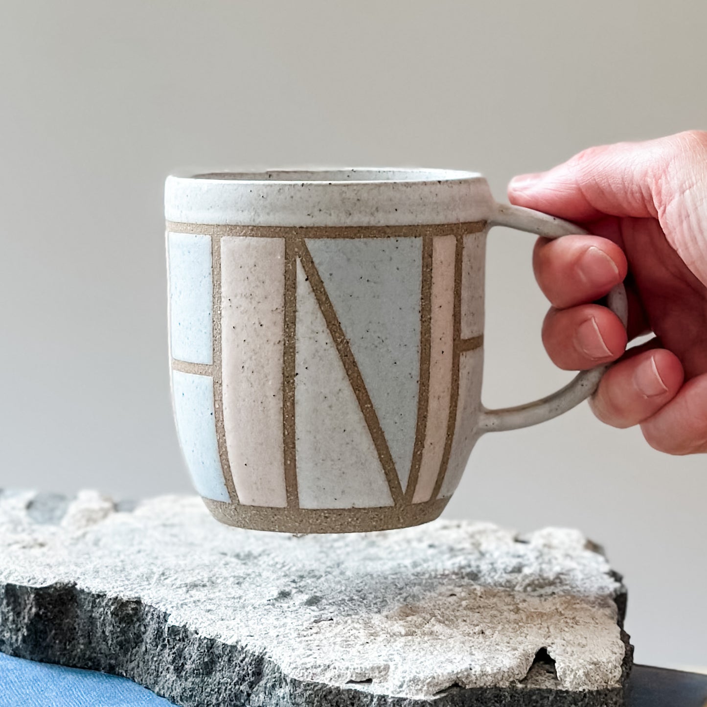 A front view of the limited edition Birdrock Ceramics geometric mug being held by a hand. The mug is painted pink, white and grey.