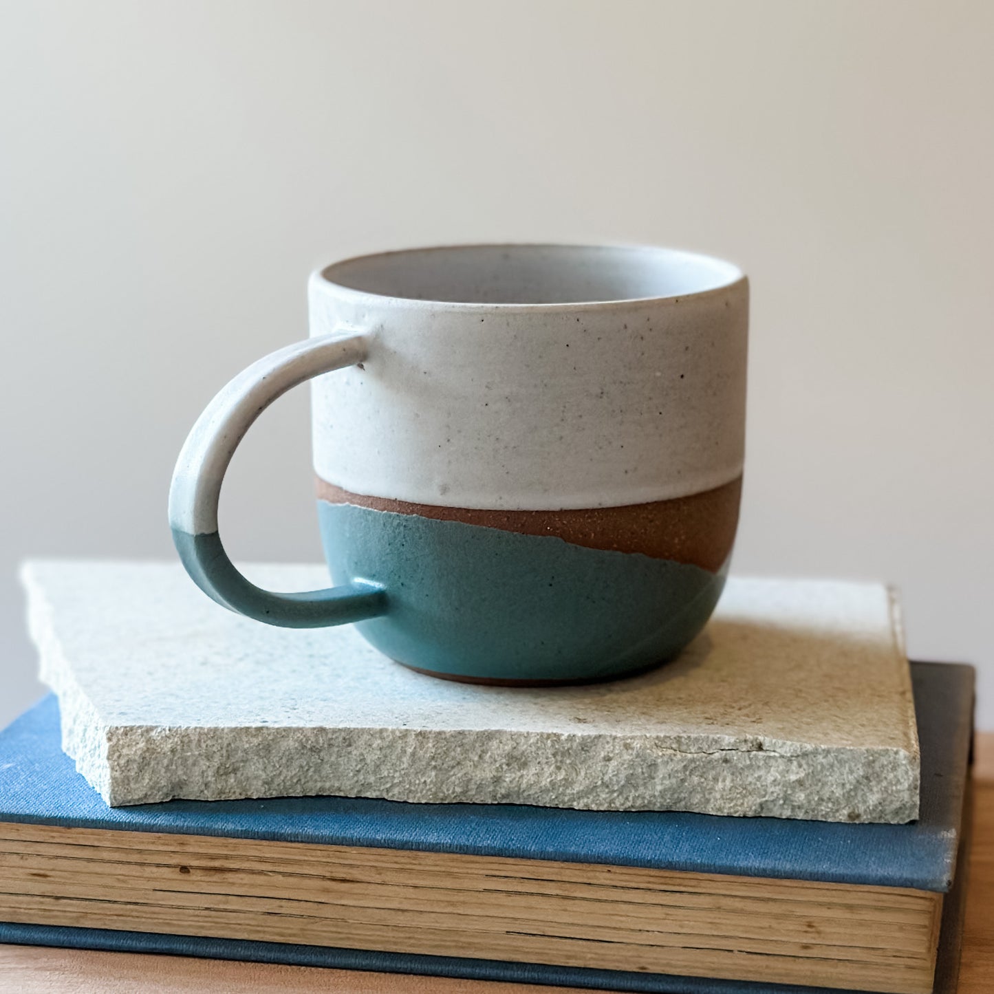 Ceramic mug with two-tone design in green, grey, and white on a stack of books
