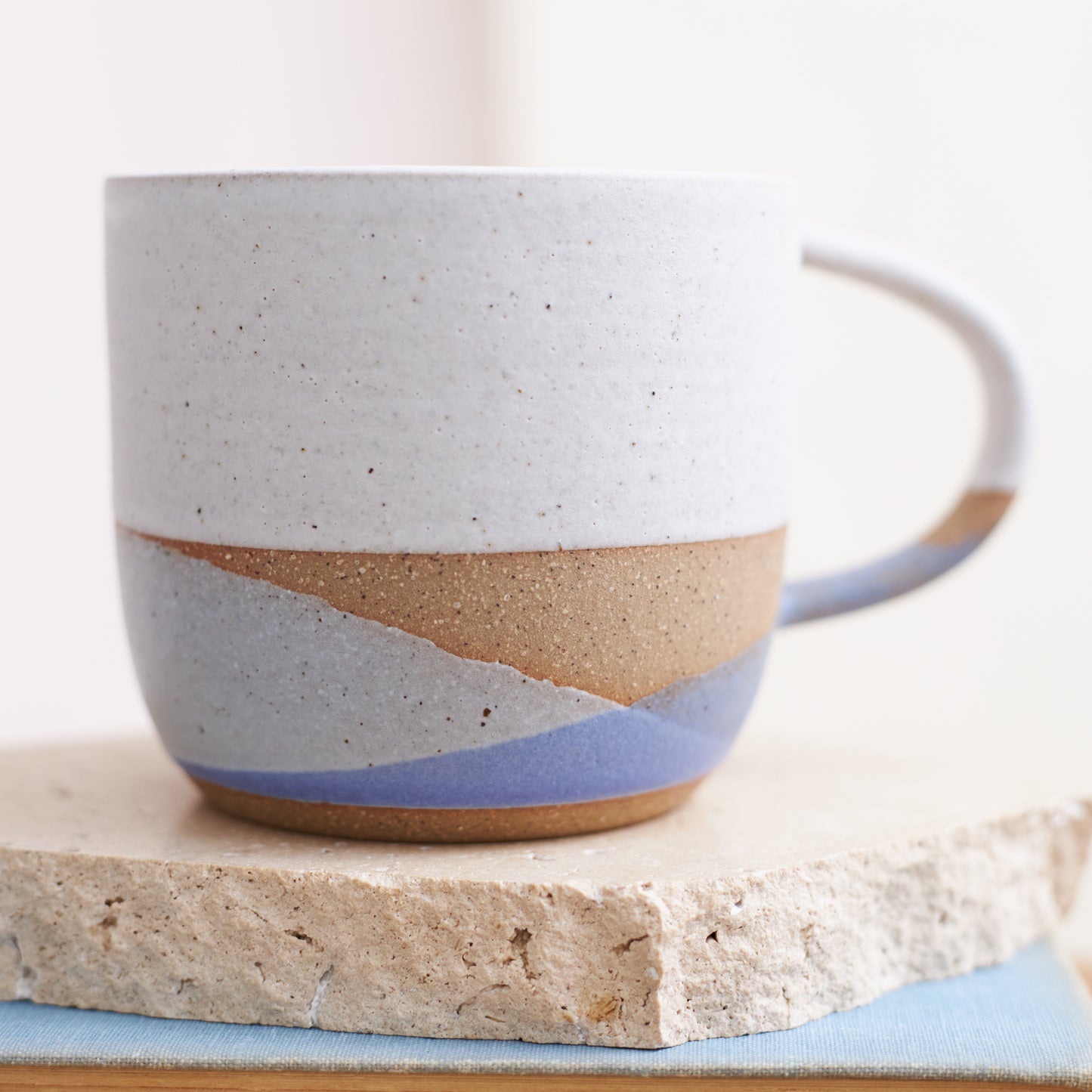 A close up image of the Tidal Handmade Ceramic Mug in a purple, grey and white glaze. The handmade mug is sitting on a cream coloured tile.