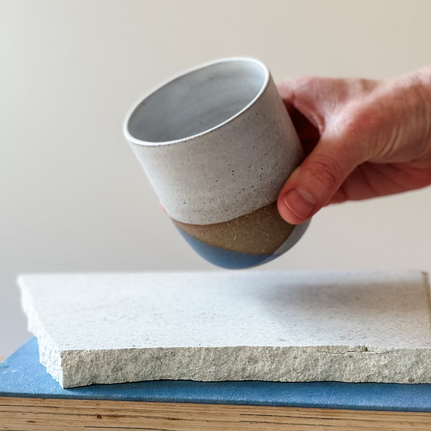 Hand holding a two-toned ceramic cup over a stack of stone slabs.