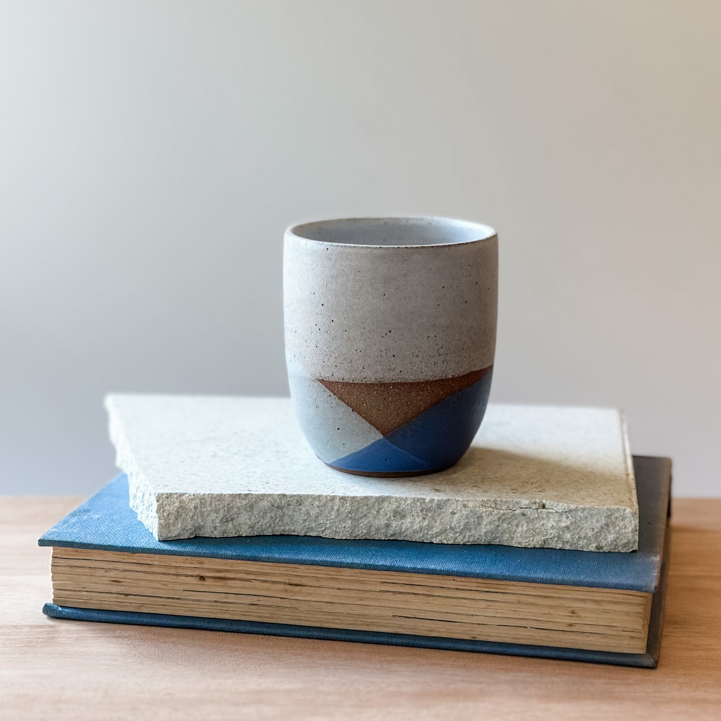 Ceramic cup with a coastal design on top of a tile and a book