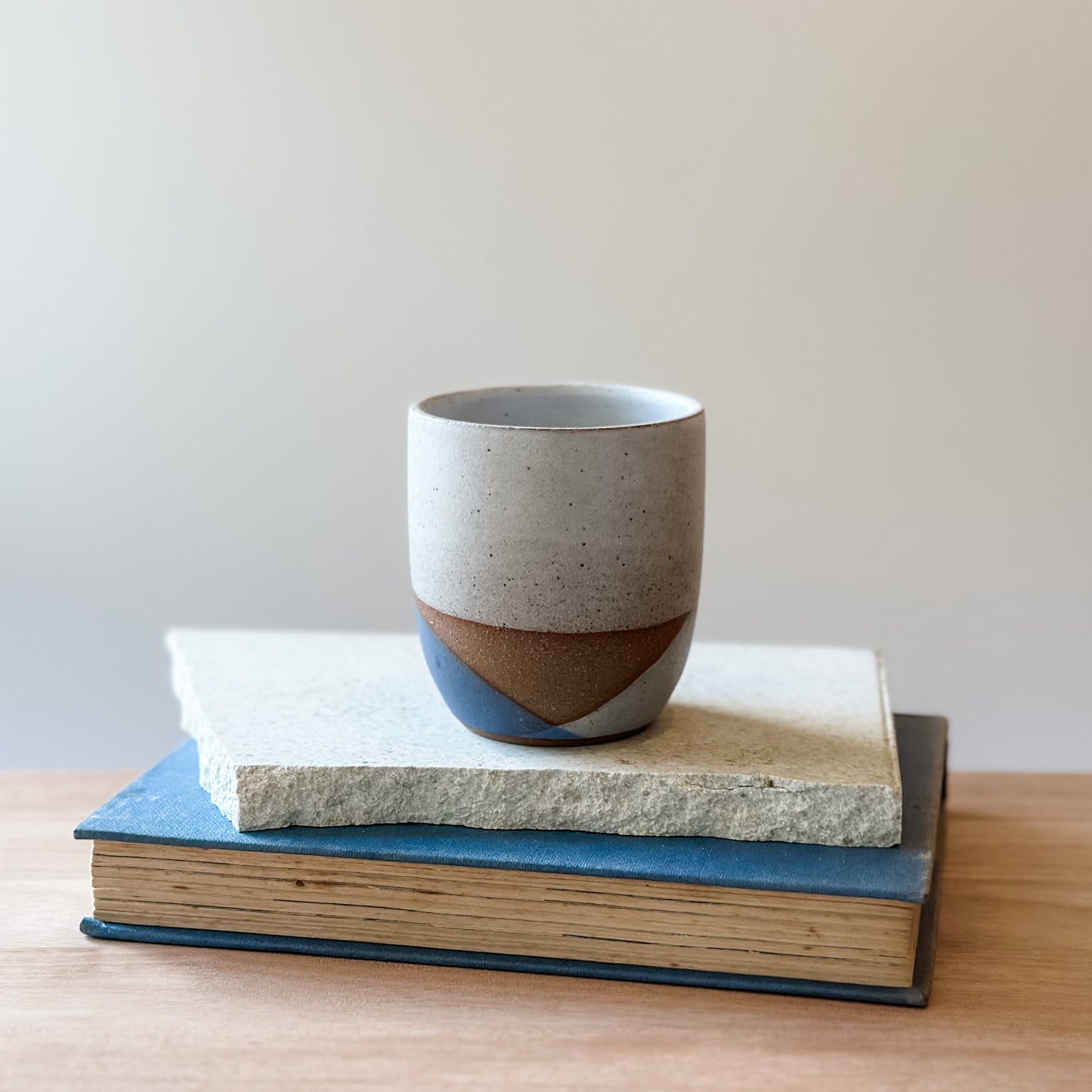 Ceramic cup with two-tone design on top of two books on a wooden surface.