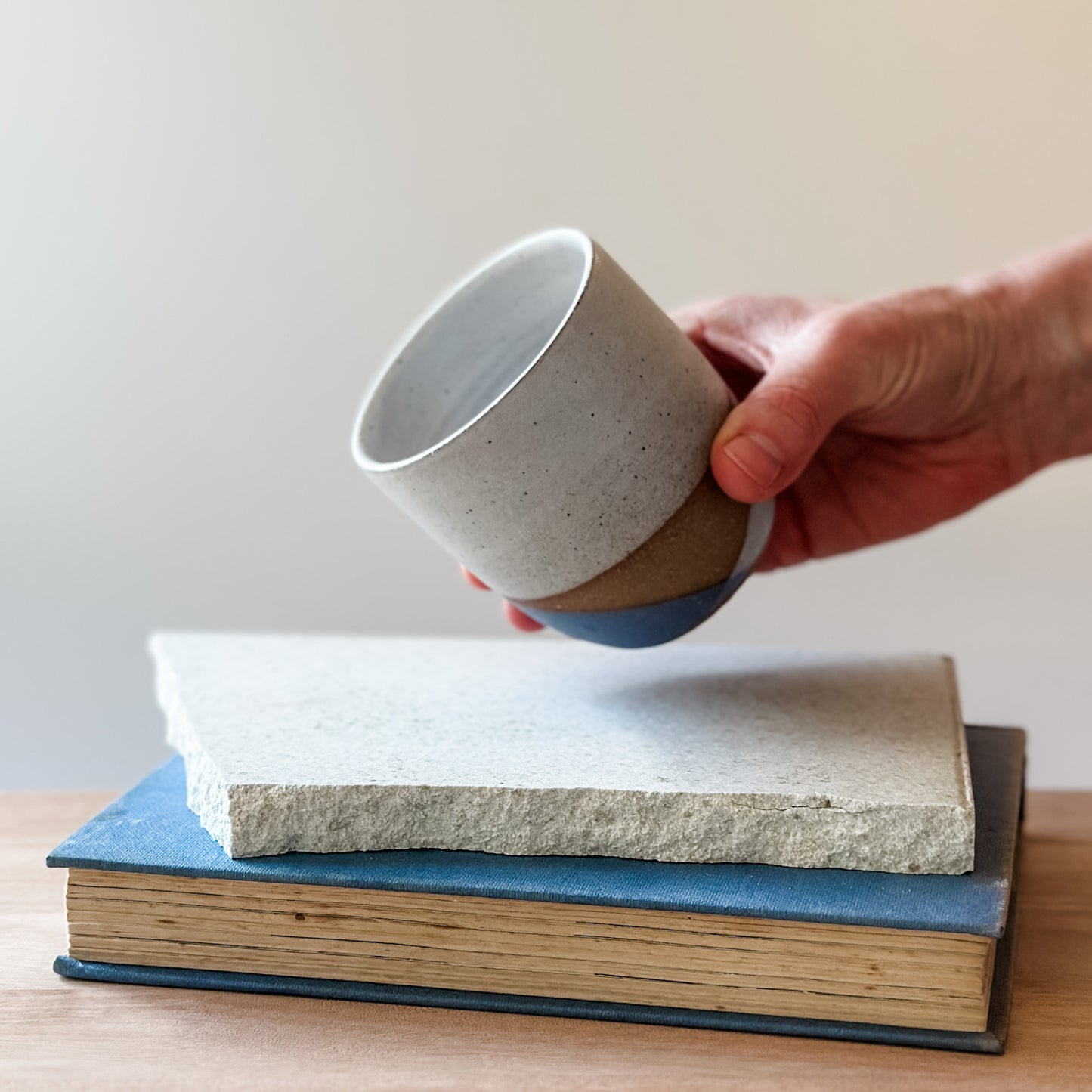 Hand holding a ceramic cup over a stack of books on a wooden surface