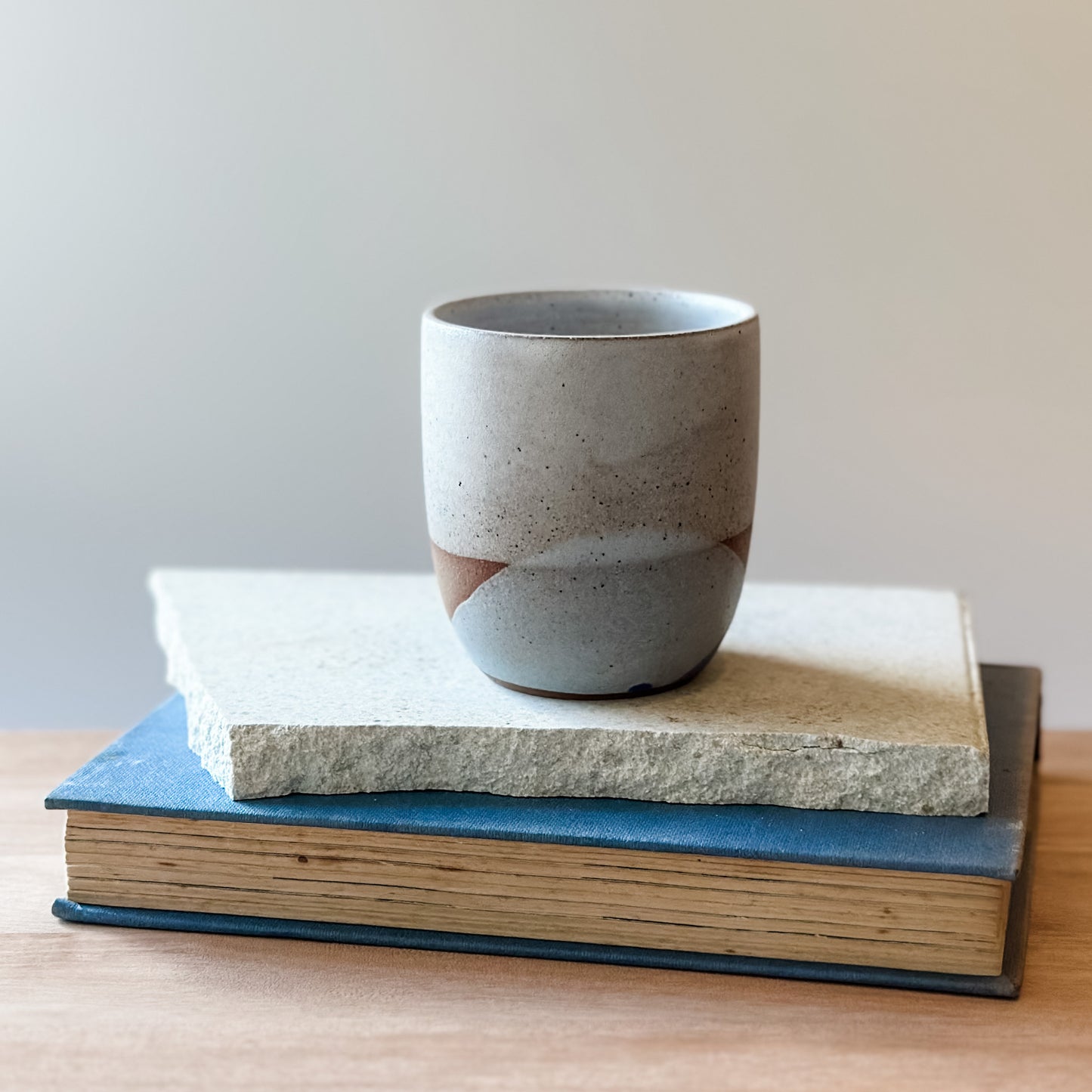 Ceramic cup on top of a tile and a book with a plain background