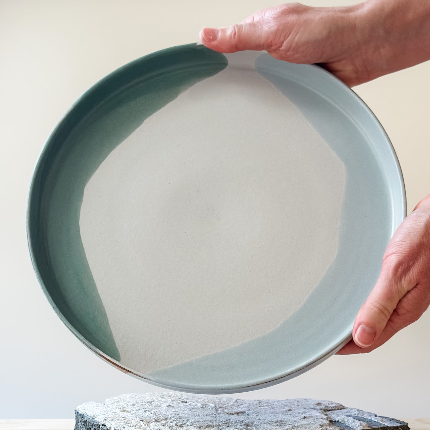 An interior view of the large Tidal Handmade Ceramic Platter being held above a tile. The handmade platter is green, blue-grey and white.