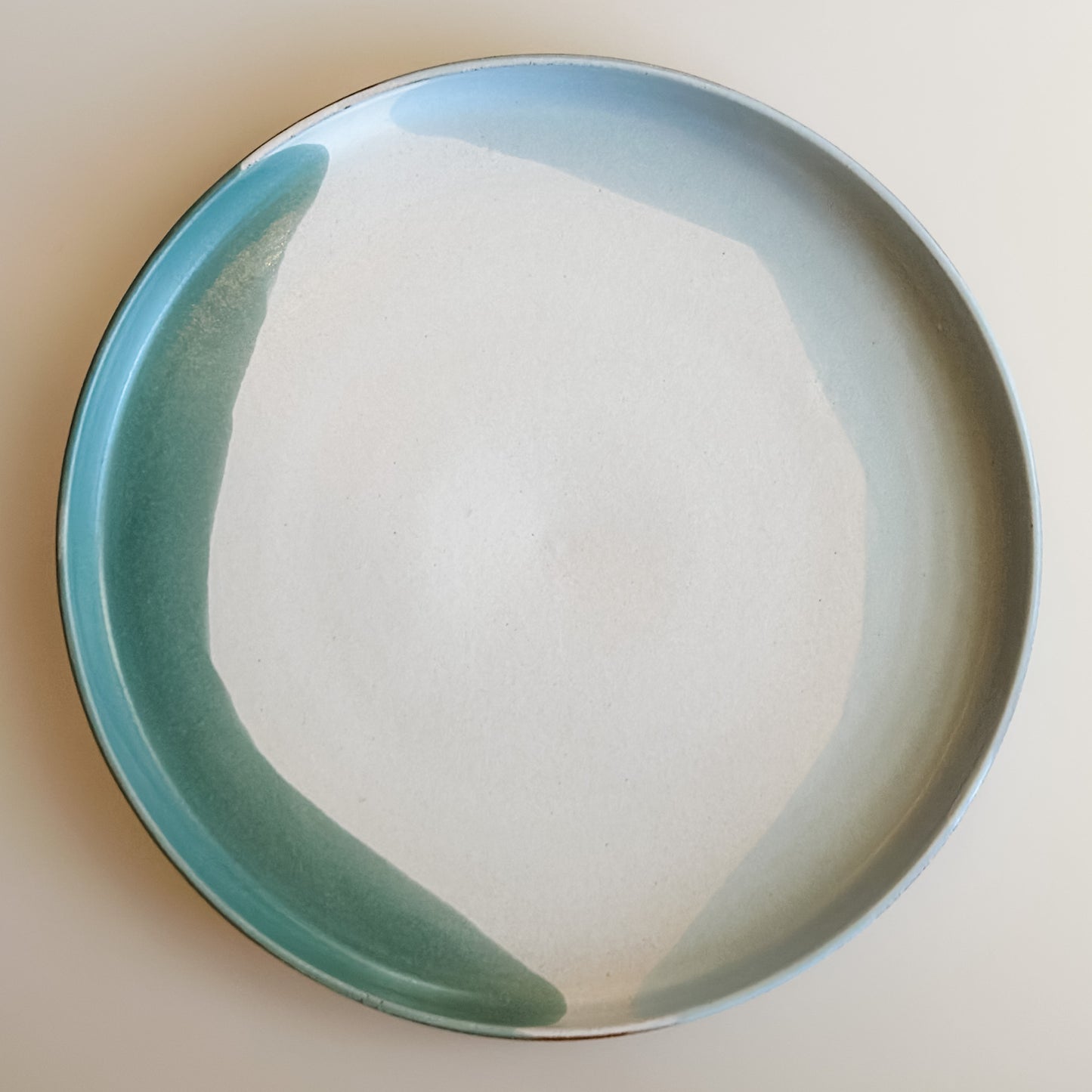 An aerial view of the large Tidal Handmade Ceramic Platter sitting on a cream background. The handmade platter is green, blue-grey and white.