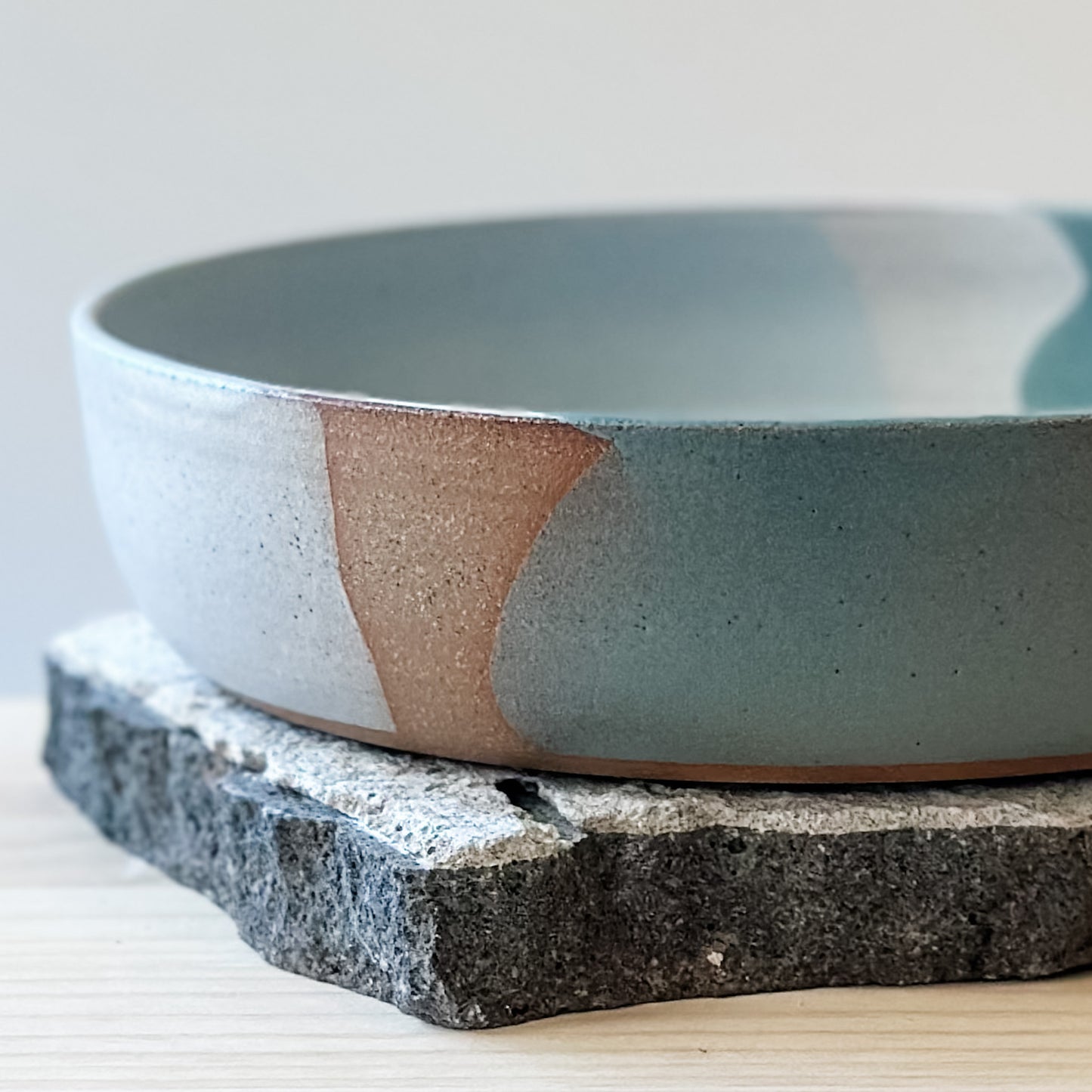 A close-up view of the Tidal Handmade Ceramic Serving Bowl. The handmade bowl sits on a tile and a wooden table.