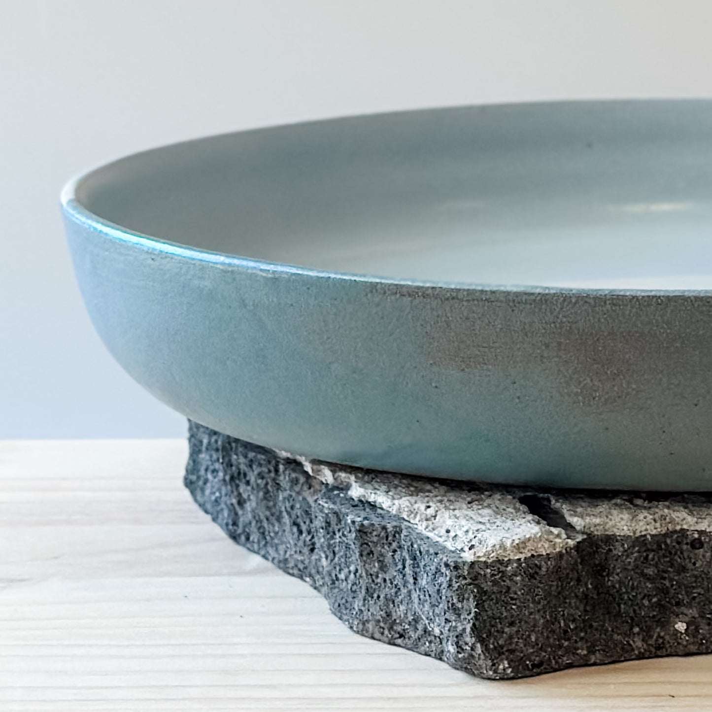 A close-up view of the side of the large Tidal Handmade Ceramic Serving Dish. The dish is green, white and blue-grey and sits on a tile and a wooden table.