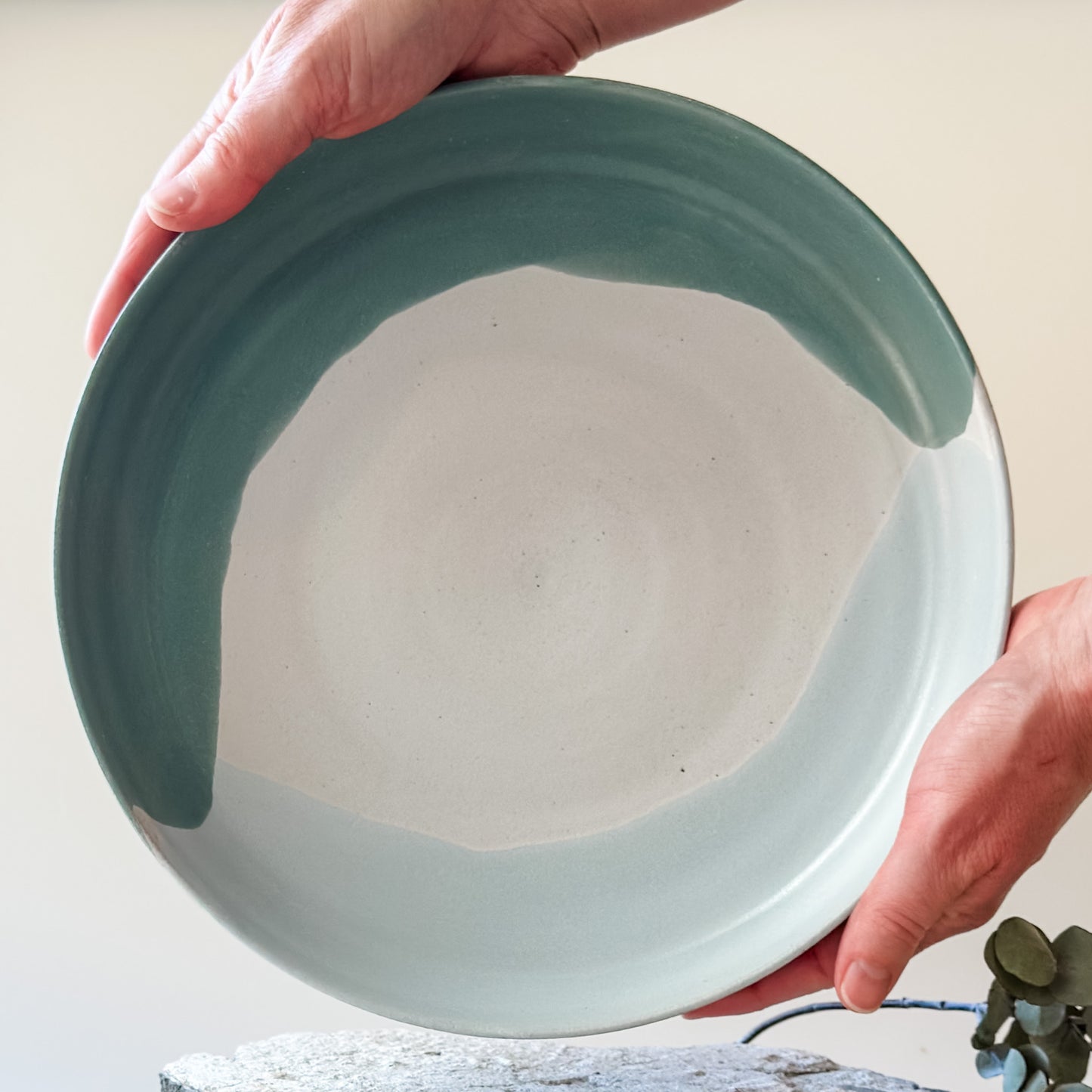 An inside view of the large Tidal Handmade Ceramic Serving Dish. The handmade dish is held with two hands above a tile and is glazed green, white and blue-grey.