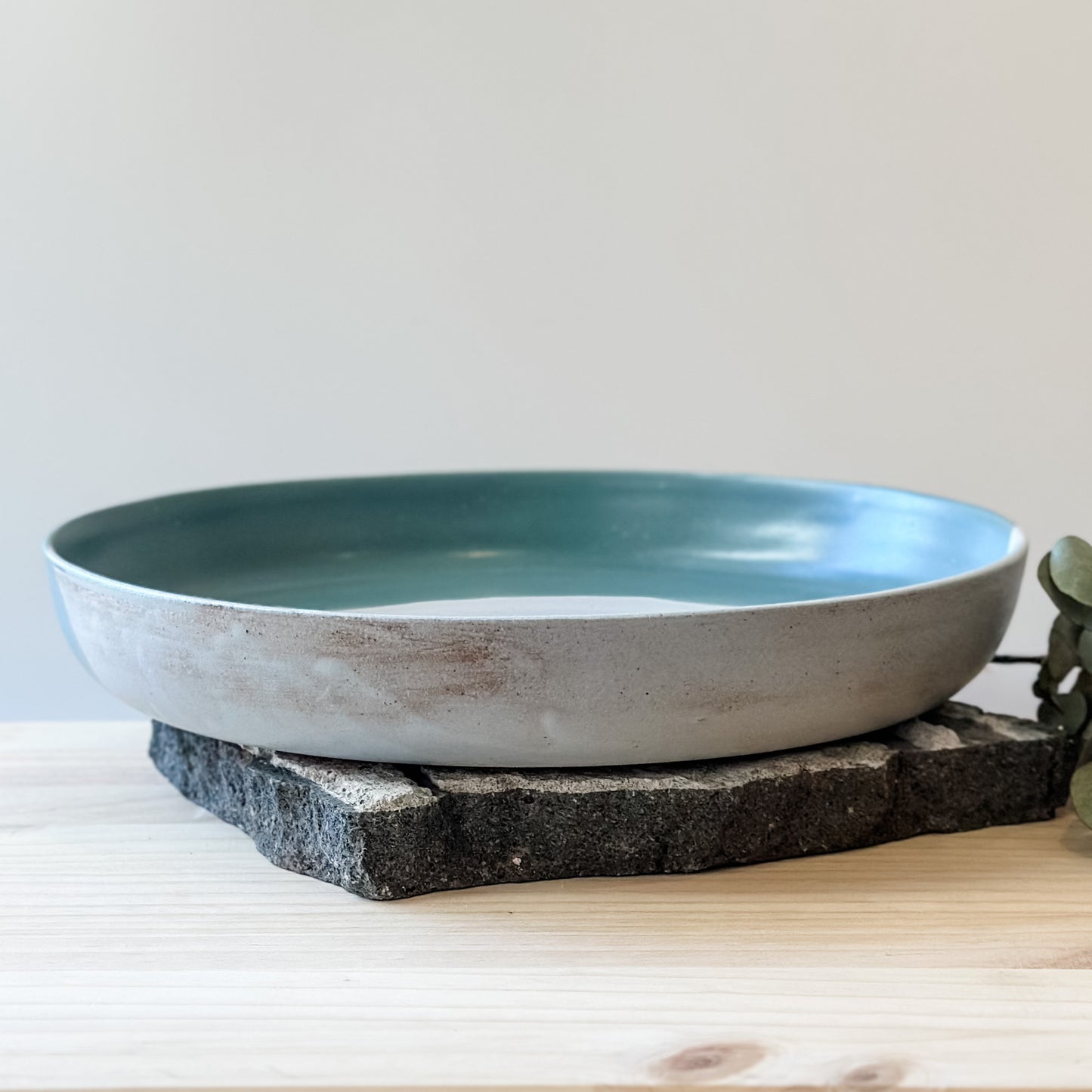 A front view of the large Tidal Handmade Ceramic Serving Dish. The dish is green, white and blue-grey and sits on a tile and a wooden table.