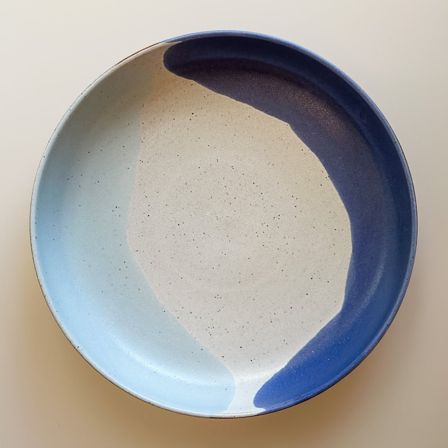 An aerial view of the Tidal Handmade Ceramic Dish in a violet purple and blue-grey glaze. The handmade dish sits on a cream background.