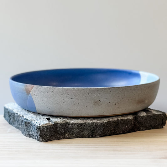 A front view of the Tidal Handmade Ceramic Dish in a violet purple and blue-grey glaze. The handmade dish sits on a tile and wooden table.