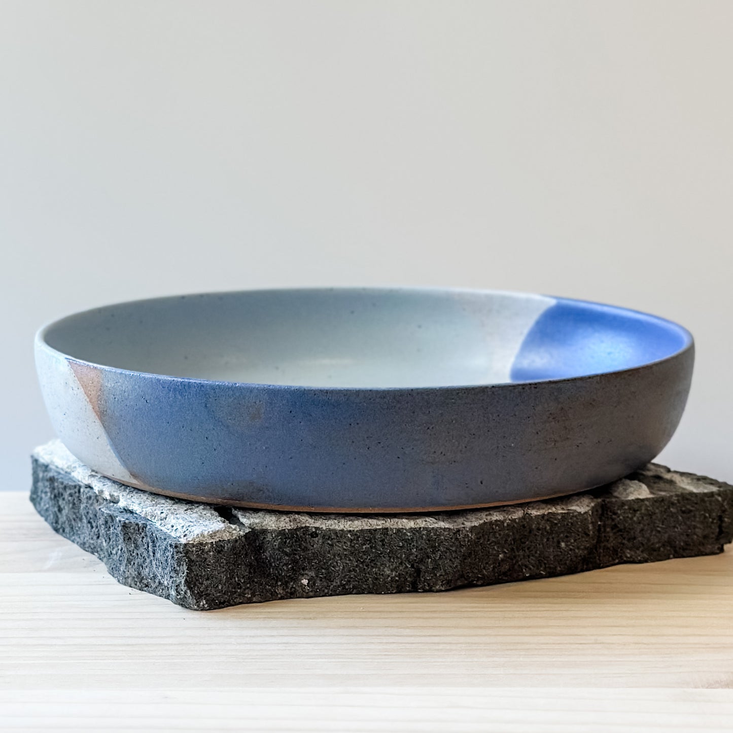 A side view of the Tidal Handmade Ceramic Dish in a violet purple and blue-grey glaze. The handmade dish sits on a tile and wooden table.