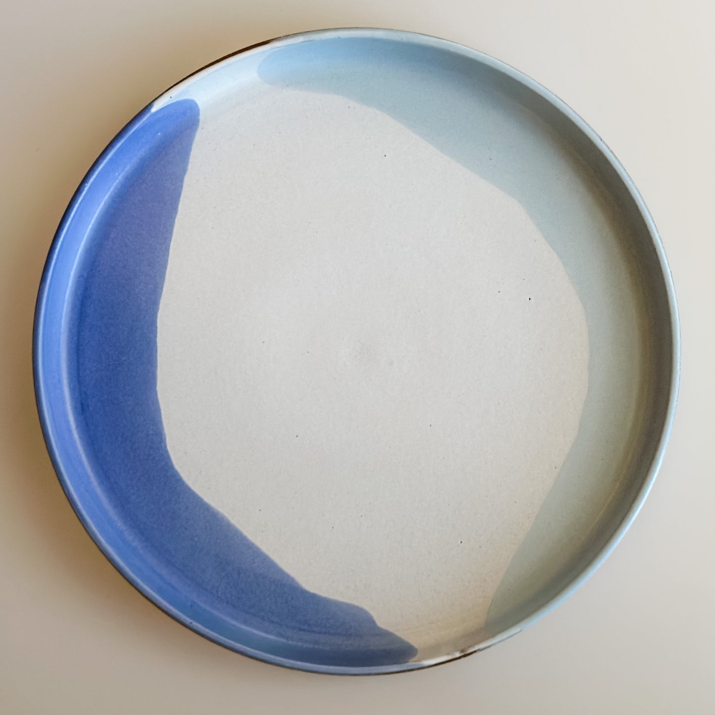 A aerial view of the medium Tidal Handmade Ceramic Platter in violet, blue-grey and white glaze. The platter sits on a cream background.