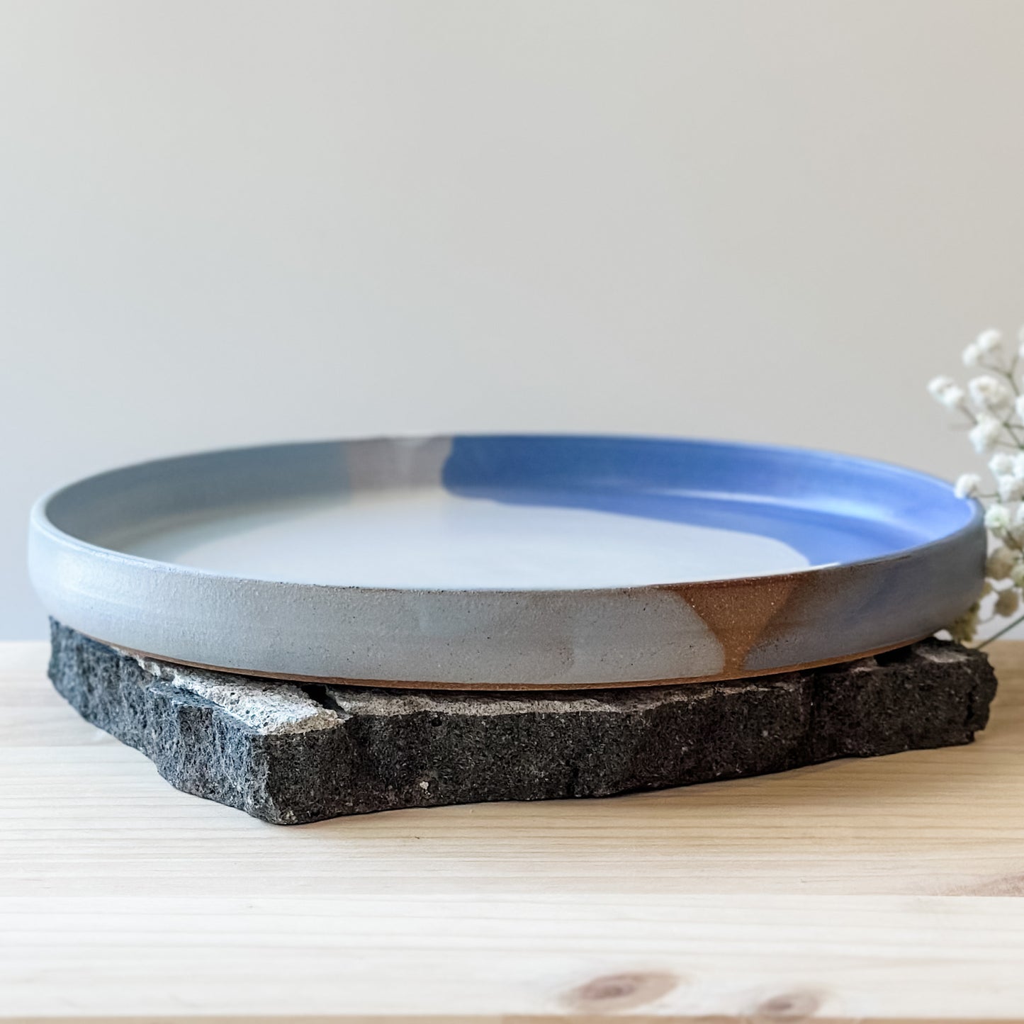 A side view of the medium Tidal Handmade Ceramic Platter in violet, blue-grey and white glaze. The platter sits on a tile and a wooden table.