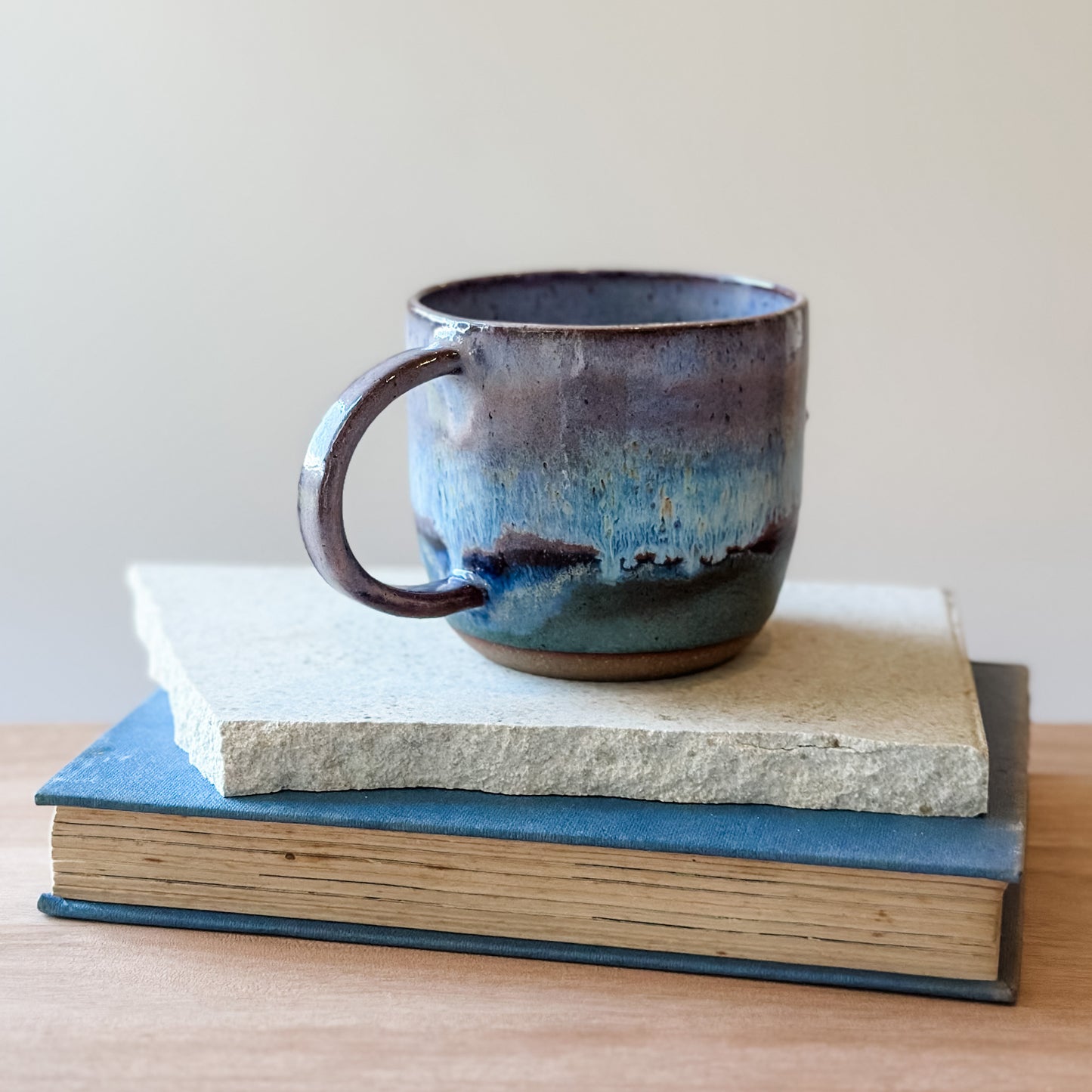Blue ceramic mug on top of a tile and a book with a plain background