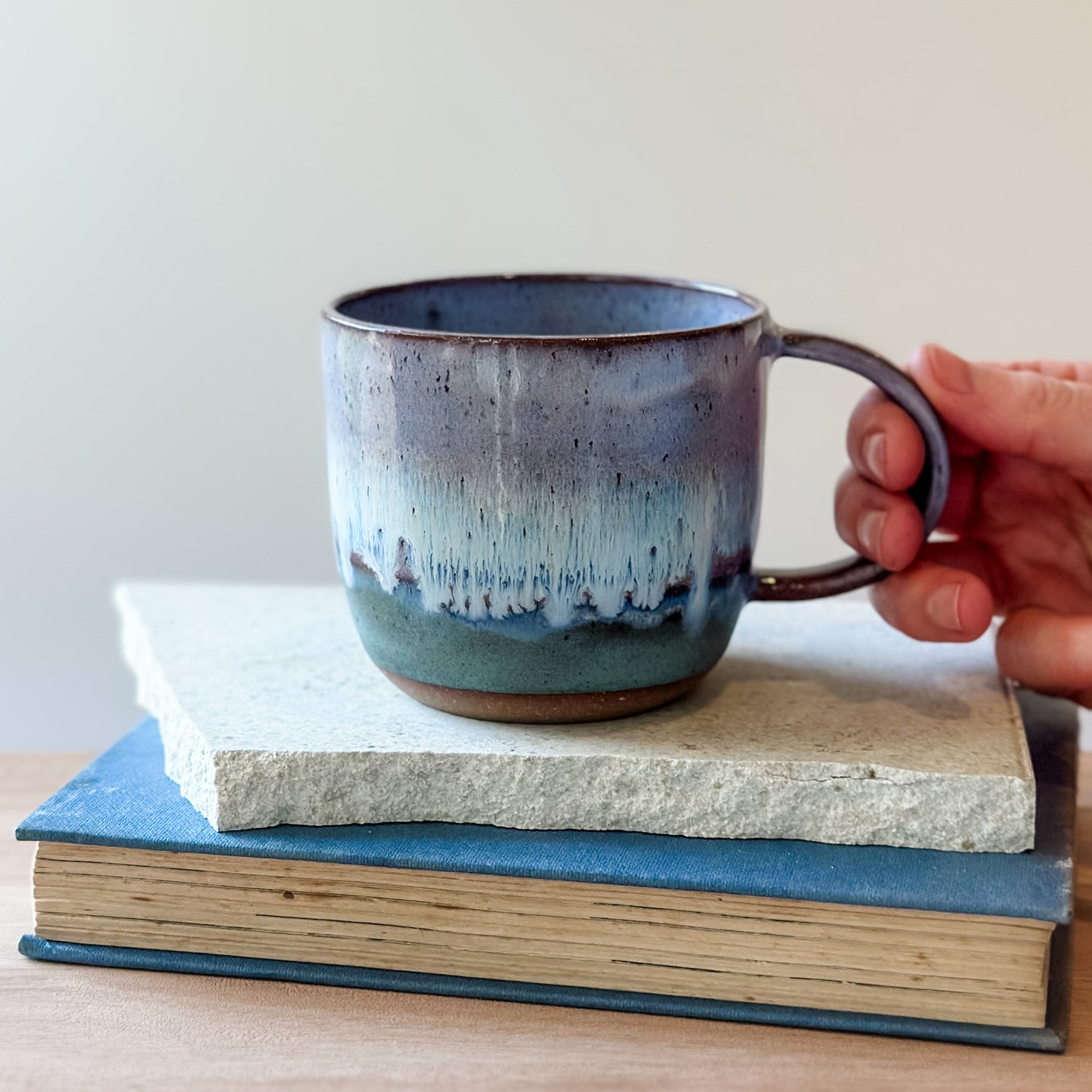 A blue ceramic mug held over a tile on a wooden table.
