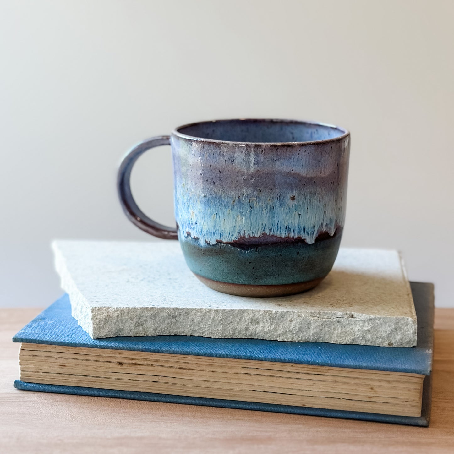 Ceramic mug with a purple and blue glaze on top of books