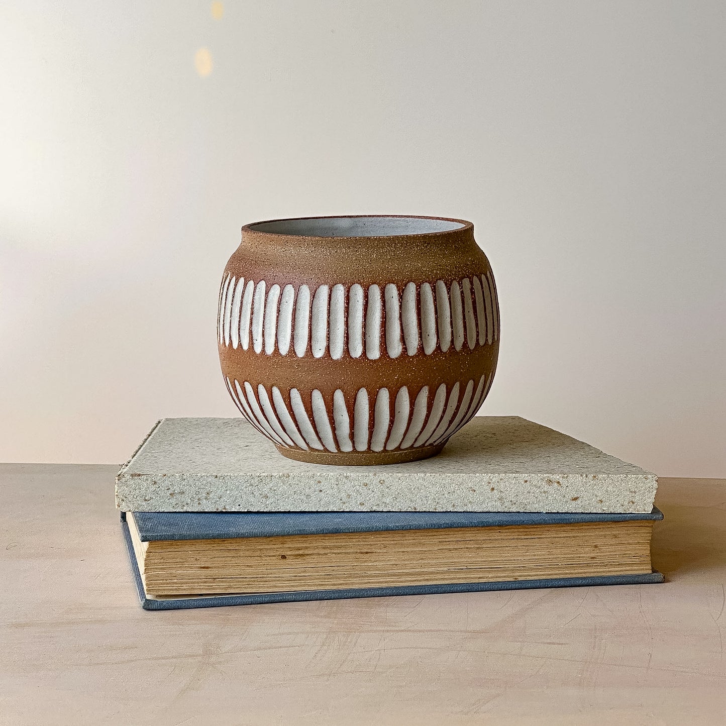 Ceramic vase with ribbed design on top of two books against a plain background