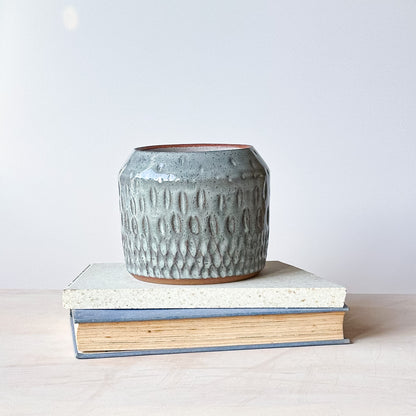 Textured ceramic pot on top of a book with a plain background