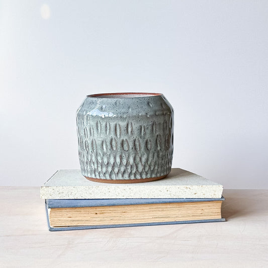 Textured ceramic pot on top of a book with a plain background