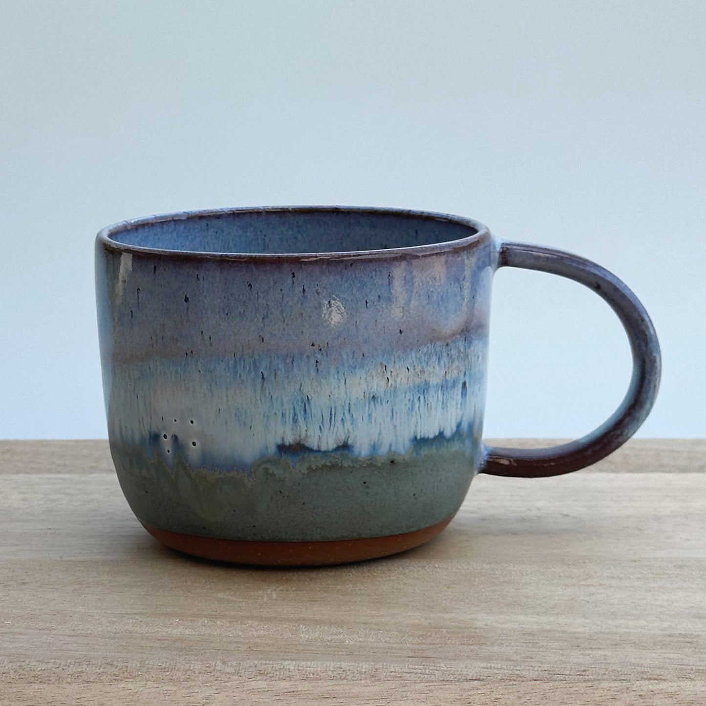 Purple and blue ceramic mug on a wooden surface with a light background