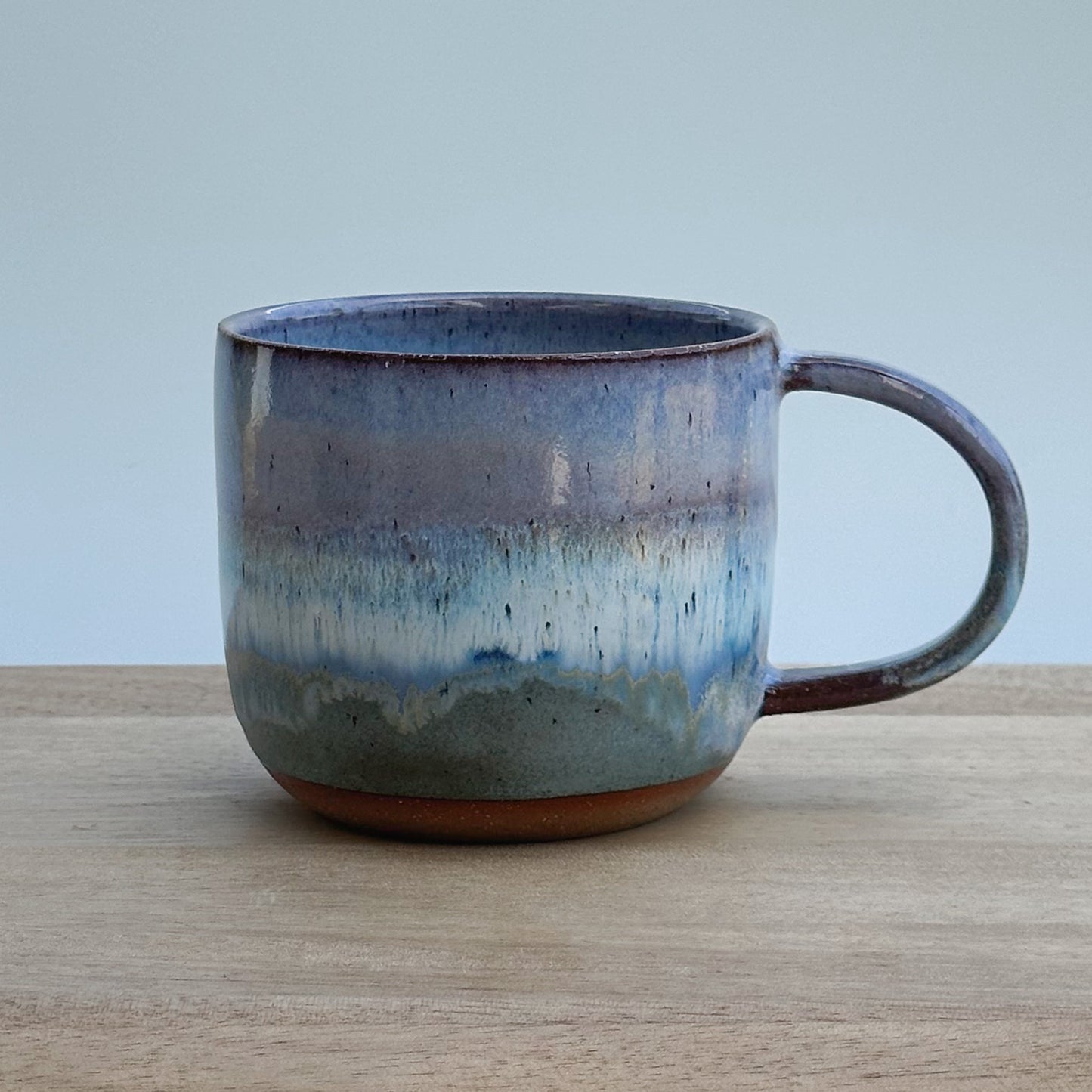 Ceramic mug with blue and brown gradient on a wooden surface and light background