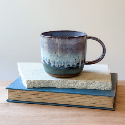 Ceramic mug with a gradient finish on top of a tile and a book.
