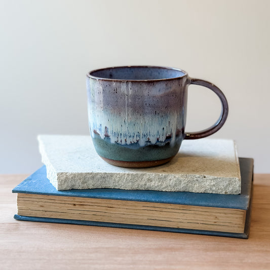 Ceramic mug with a gradient finish on top of a tile and a book.