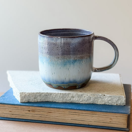 Ceramic mug with blue gradient on top of a tile and a book