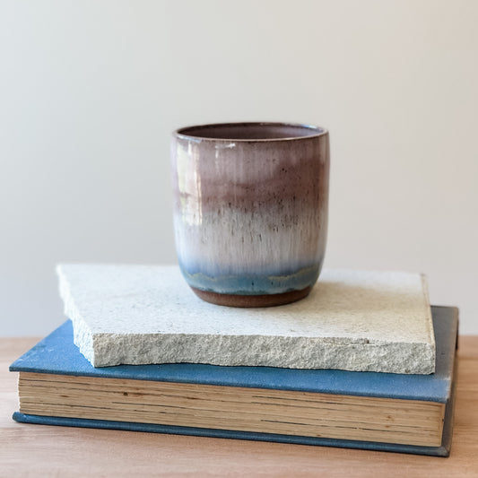 Ceramic cup on top of a tile and a book with a plain background