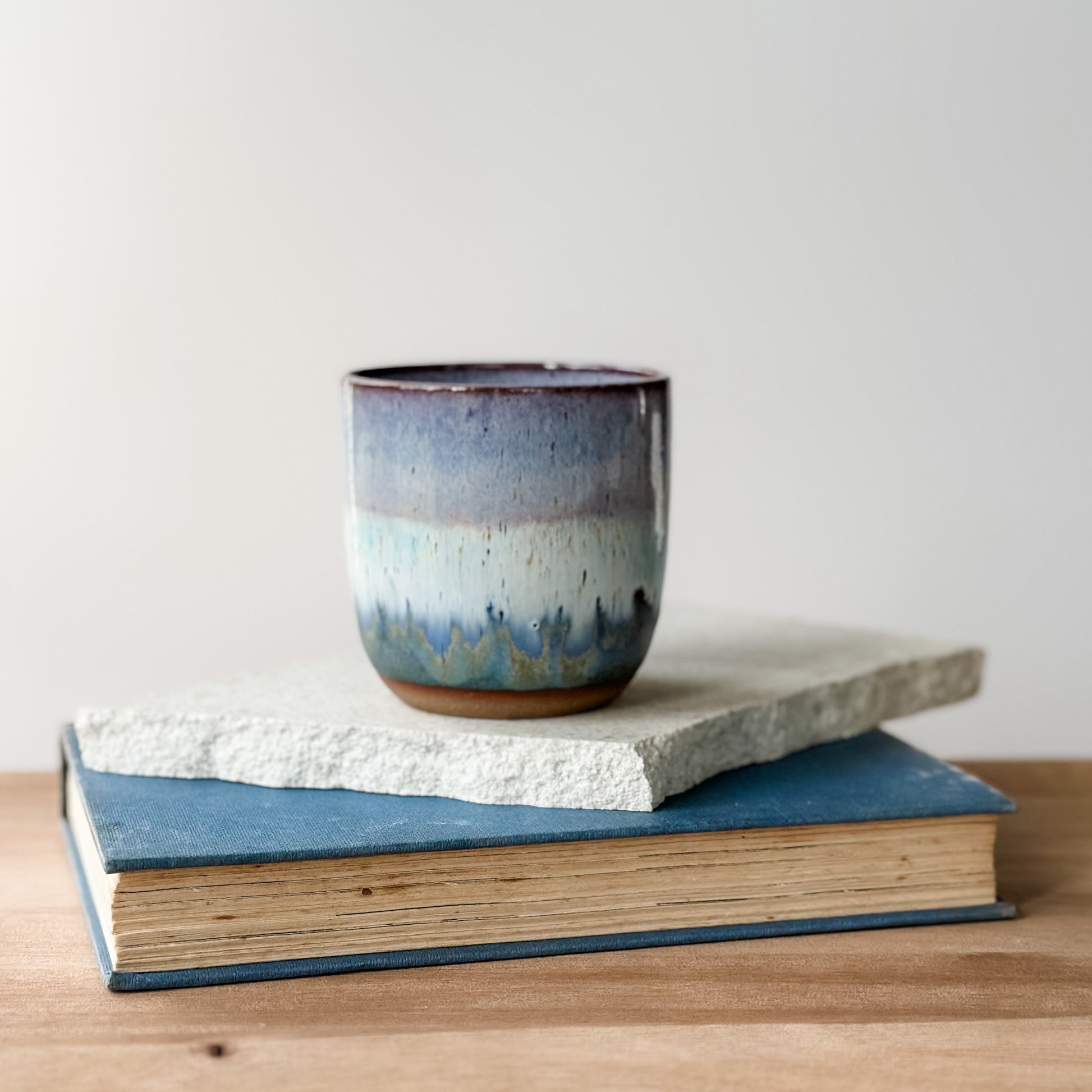 Ceramic mug with a textured surface on top of a book on a wooden surface.