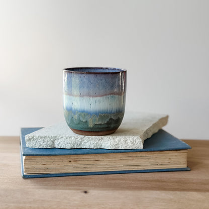 Ceramic cup with blue and purple glaze on a stack of books