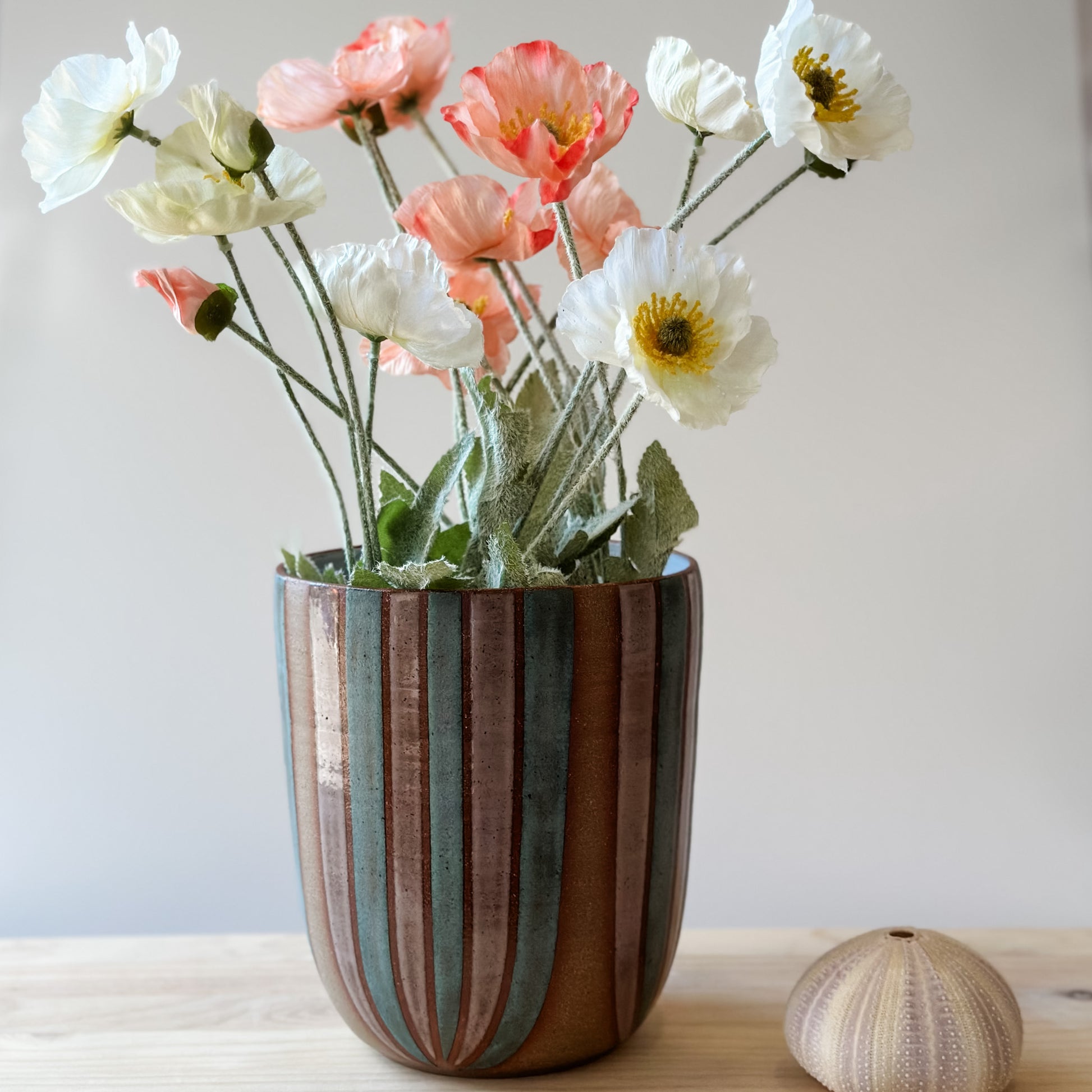 A large handmade ceramic bouquet vase sits on a table. The ceramic vase is hand-painted in blush pink and denim blue glaze. The bouquet vase is displaying flowers in pastel colours.