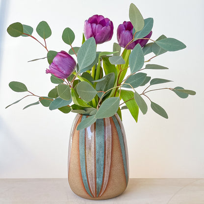 Decorative vase with striped pattern holding purple tulips and green leaves on a light background