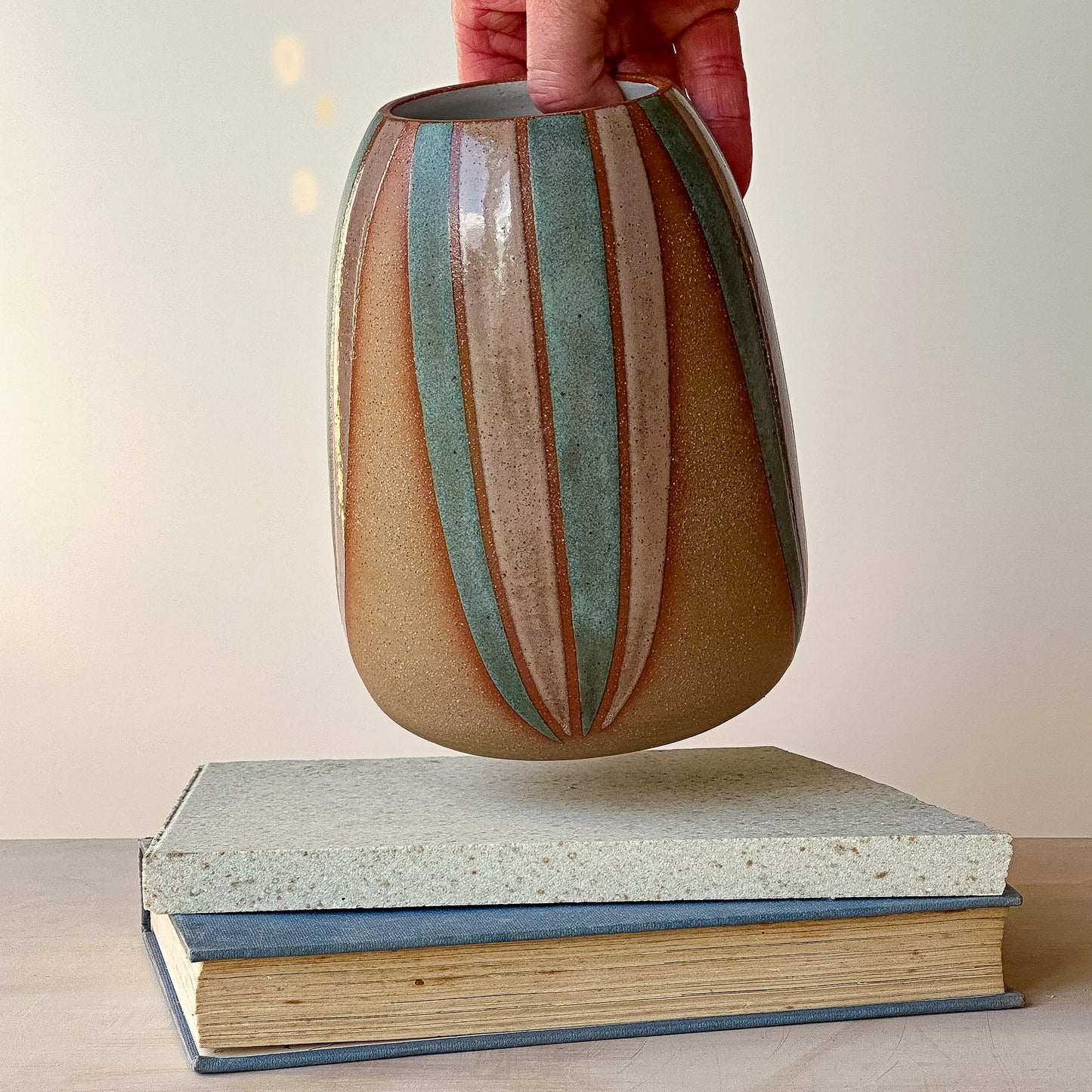 Ceramic vase with striped design held above two stacked books on a neutral background