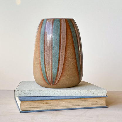 Ceramic vase with striped design on top of two books against a light background