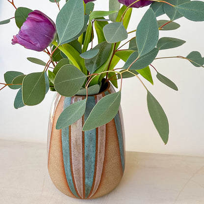 Ceramic vase with striped design and flowers held above two stacked books on a neutral background