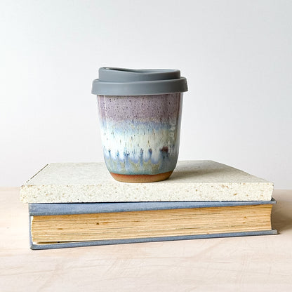 A take-away keep cup with a grey lid on a tile.