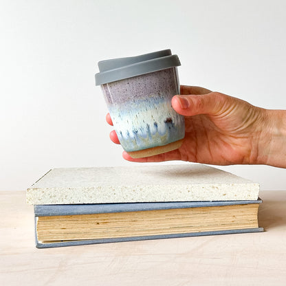 A hand holding a take-away coffee cup over a tile