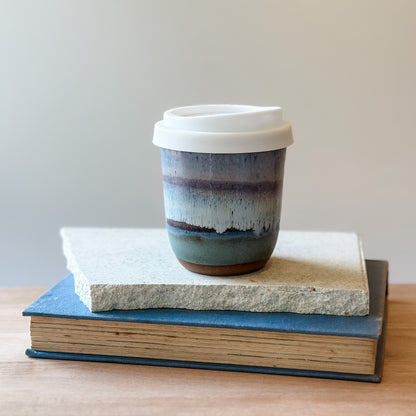 Ceramic coffee cup with a white lid on top of books with a plain background