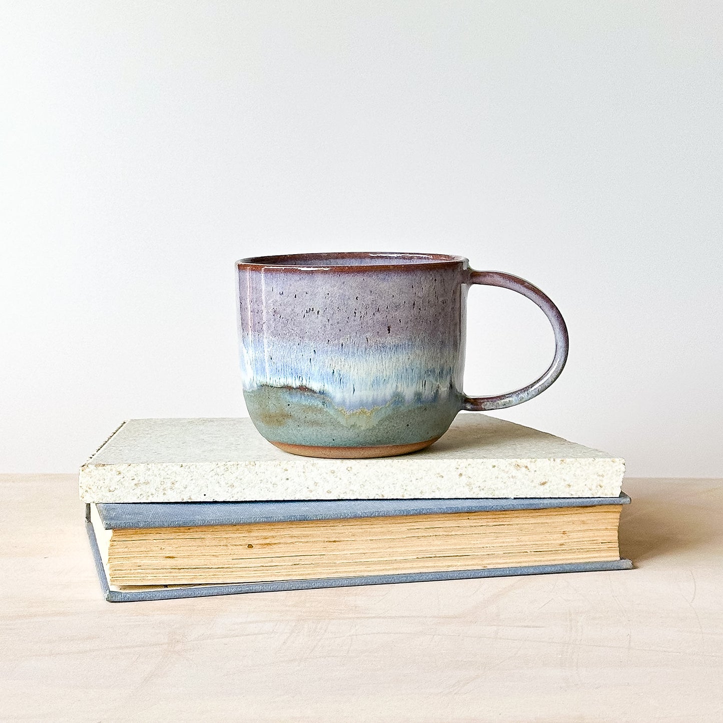 Ceramic mug with a speckled design on top of two books against a white background