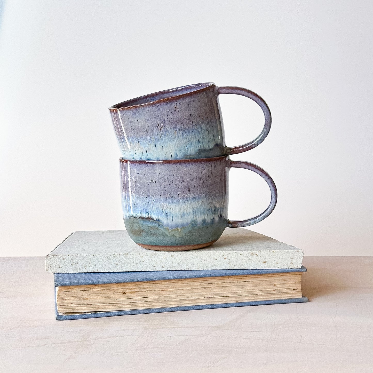 Two ceramic mugs stacked on top of each other with a plain background