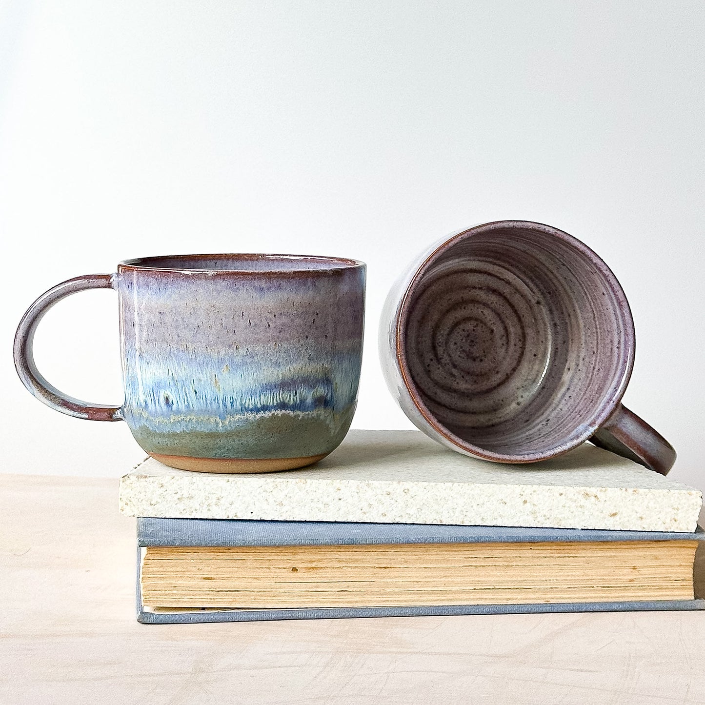Two ceramic mugs on a stack of books with a plain background