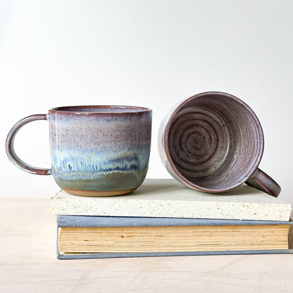 Two ceramic mugs on a stack of books with a plain background