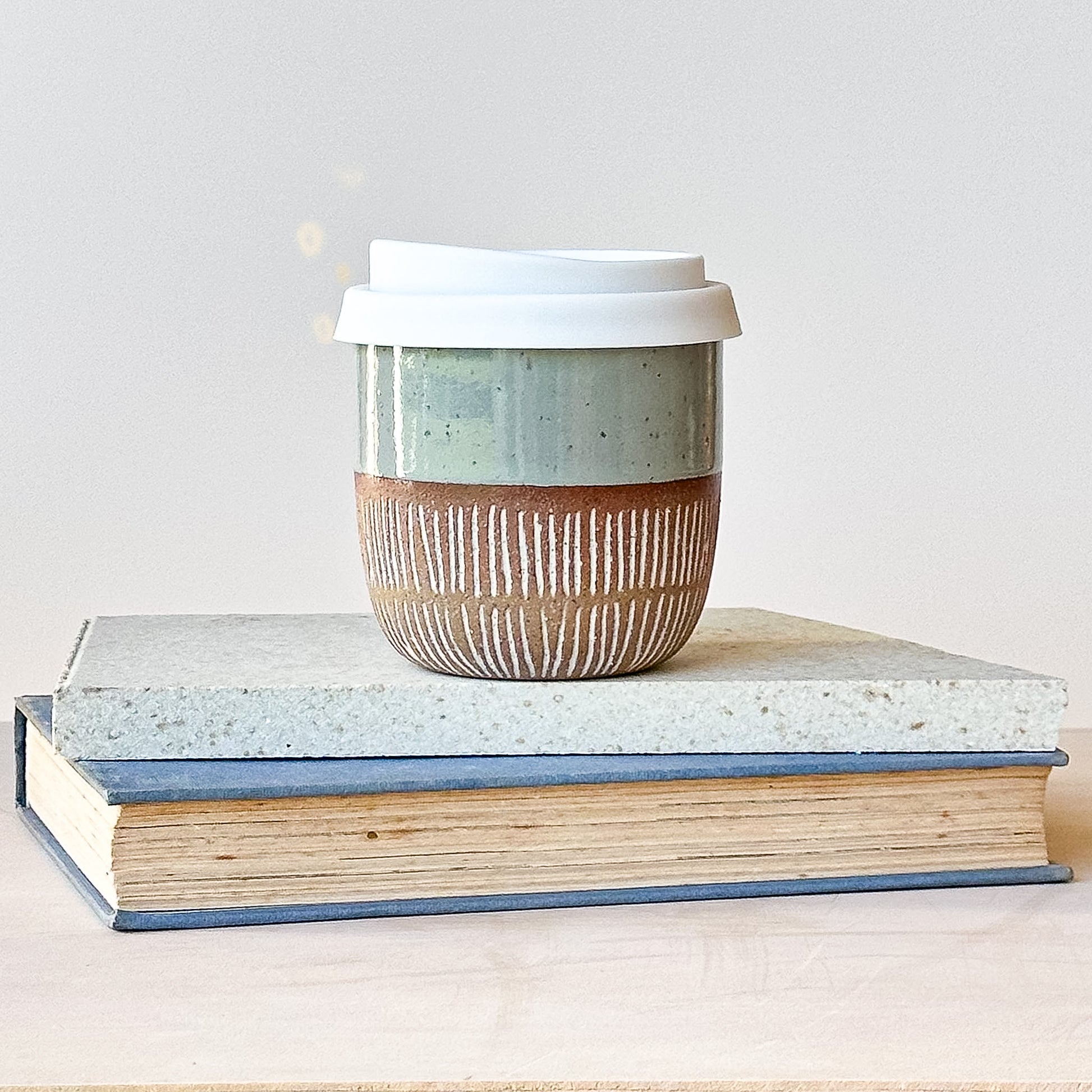 Ceramic coffee cup with a lid on top of two stacked books against a light background