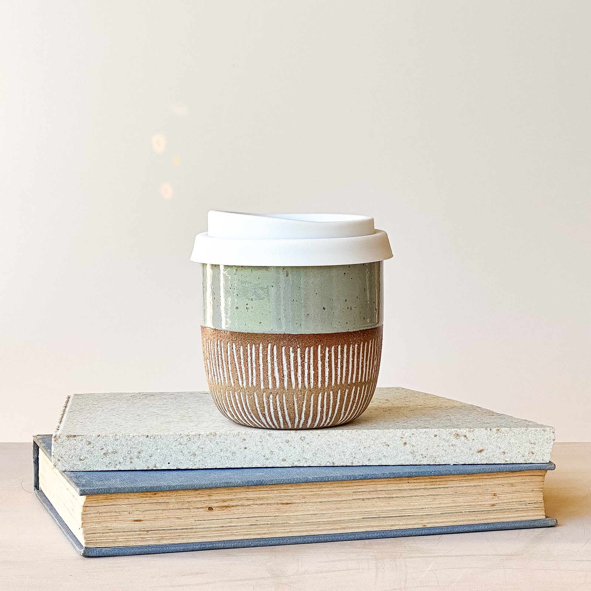 Ceramic coffee cup with a lid on top of two books against a light background