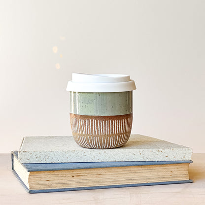 Ceramic coffee cup with a lid on top of two books against a light background