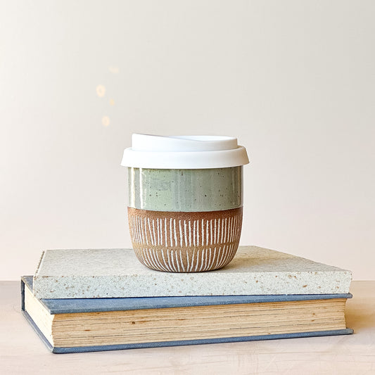 Ceramic coffee cup with a lid on top of two books against a light background