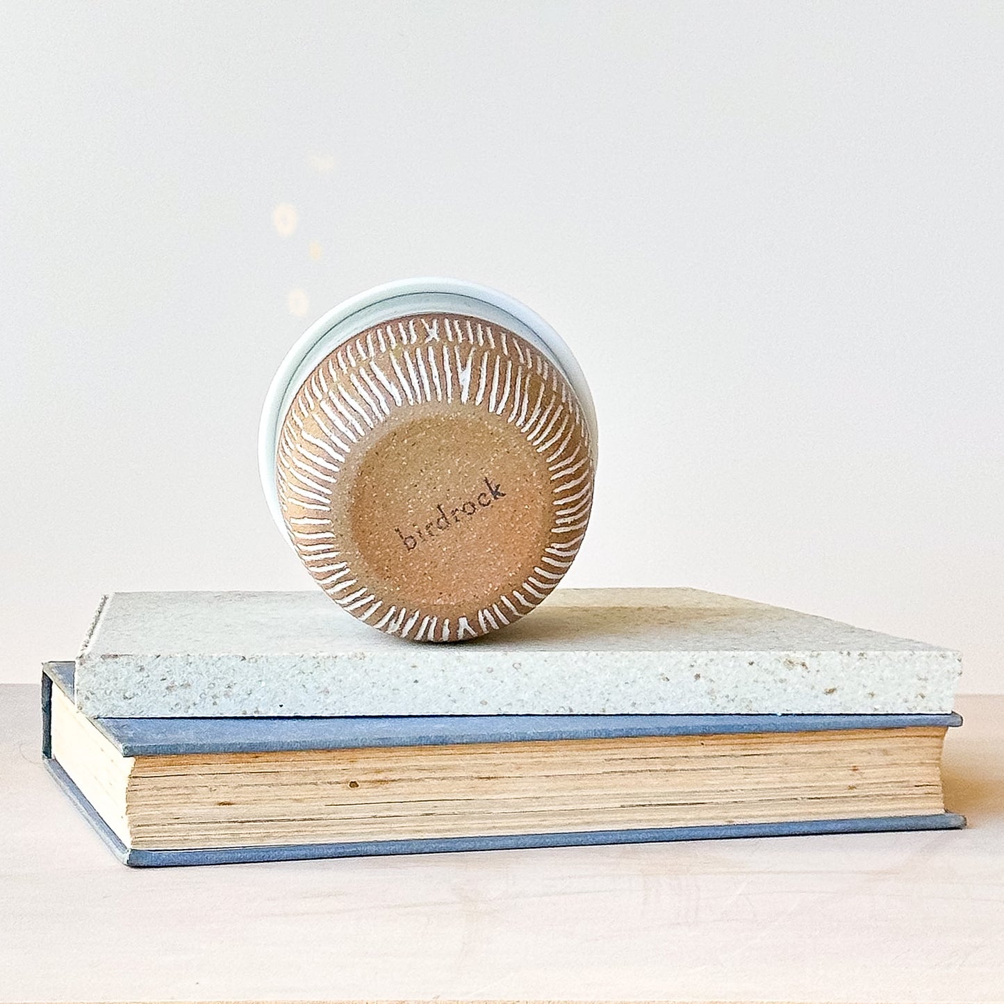 Base view of a ceramic keep cup on top of a stack of books with a light background
